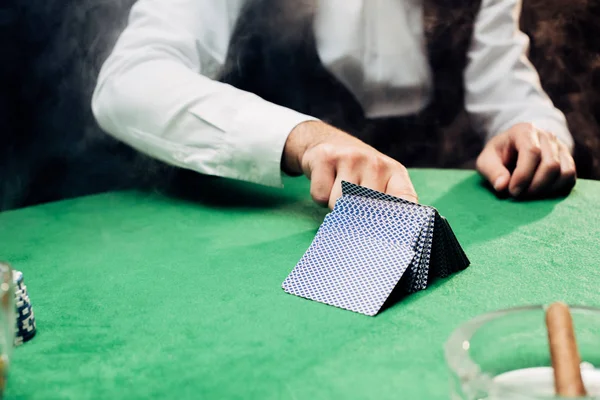 KYIV, UKRAINE - AUGUST 20, 2019: cropped view of croupier touching playing cards on black — Stock Photo