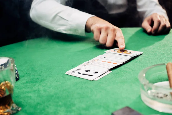 KYIV, UKRAINE - AUGUST 20, 2019: cropped view of croupier pointing with finger at playing cards on black — Stock Photo