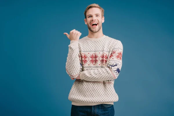 Homem rindo em camisola de inverno apontando para algo isolado em azul — Fotografia de Stock