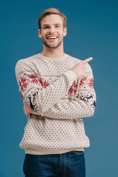 Uomo sorridente in maglione invernale che punta a qualcosa di isolato sul blu — Foto stock
