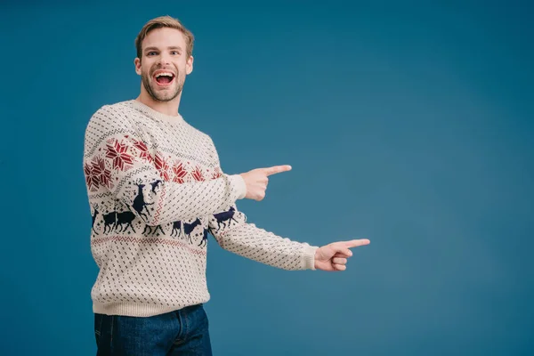 Збуджений чоловік взимку светр вказує на щось ізольоване на синьому — стокове фото