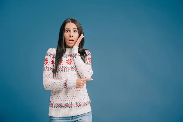 Beautiful shocked woman posing in winter sweater isolated on blue — Stock Photo