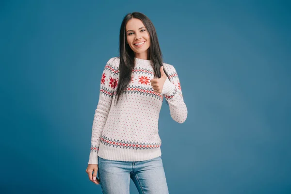 Smiling woman in winter sweater showing thumb up isolated on blue — Stock Photo