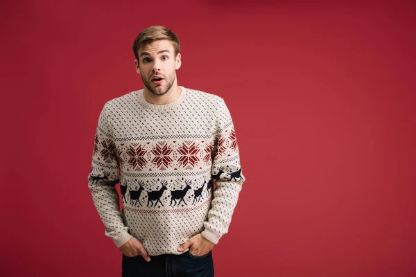 Schöner überraschter Mann posiert in Winterpullover isoliert auf Rot — Stockfoto