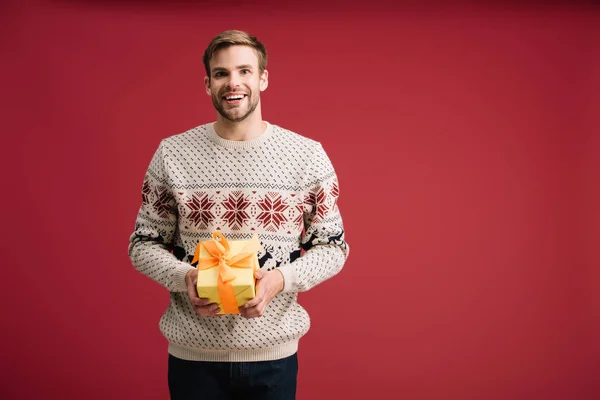 Schöner lächelnder Mann mit Weihnachtsgeschenk isoliert auf rot — Stockfoto