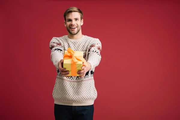 Bonito alegre homem segurando Natal presente isolado no vermelho — Fotografia de Stock