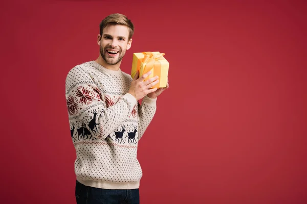 Fröhlicher Mann hält Weihnachtsgeschenk isoliert auf rot — Stockfoto