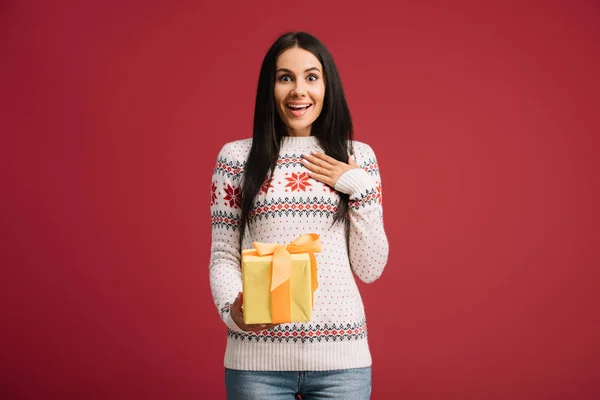 Hermosa mujer sorprendida sosteniendo regalo de Navidad aislado en rojo - foto de stock