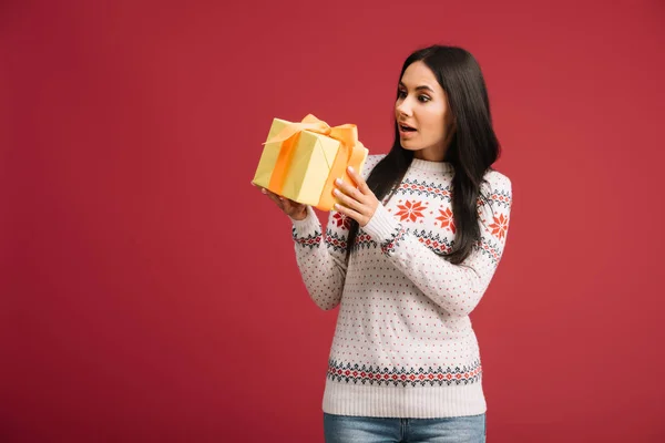 Beautiful shocked woman holding christmas present isolated on red — Stock Photo