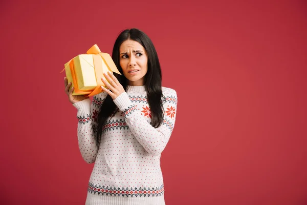Bela mulher preocupada segurando Natal presente isolado no vermelho — Fotografia de Stock