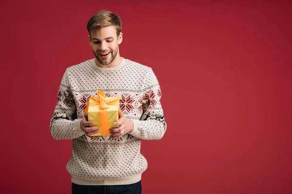 Excited handsome man holding christmas gift box isolated on red — Stock Photo