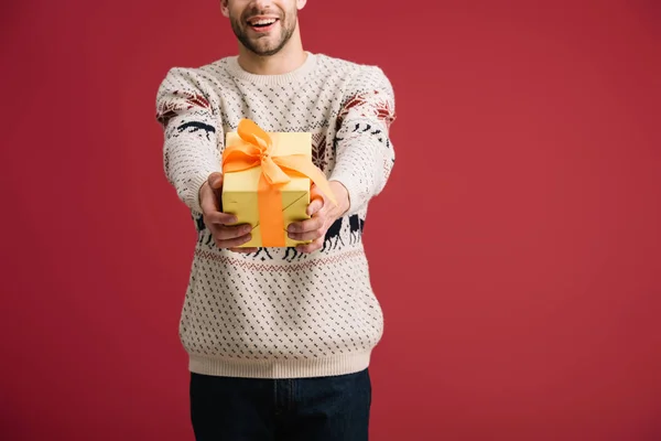 Vista recortada del hombre guapo sosteniendo caja de regalo de Navidad aislado en rojo - foto de stock