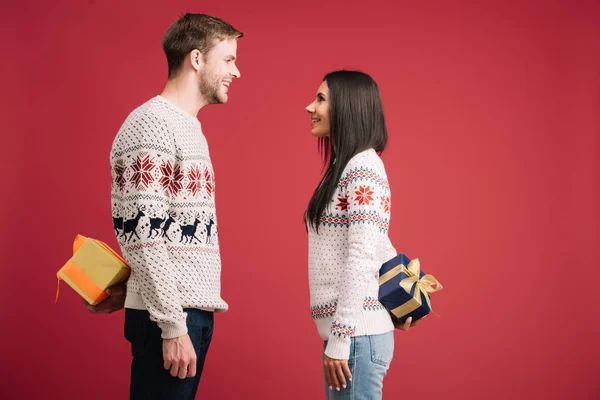 Sonriente pareja ocultando regalos de Navidad aislados en rojo — Stock Photo