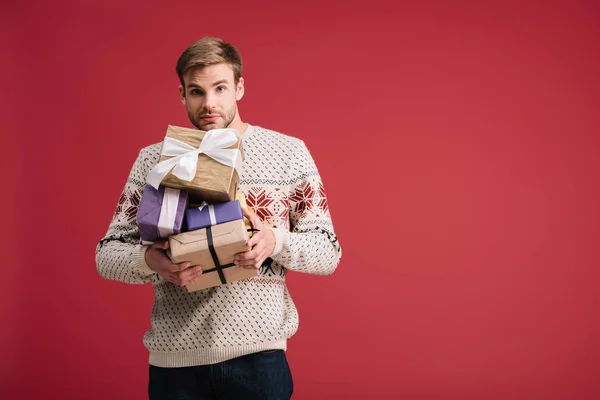 Handsome young man holding christmas presents isolated on red — Stock Photo