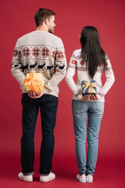 Vue arrière du couple cachant des cadeaux de Noël isolés sur rouge — Photo de stock