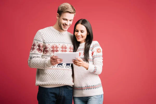 Sonriente pareja en suéteres de invierno utilizando tableta digital aislada en rojo - foto de stock