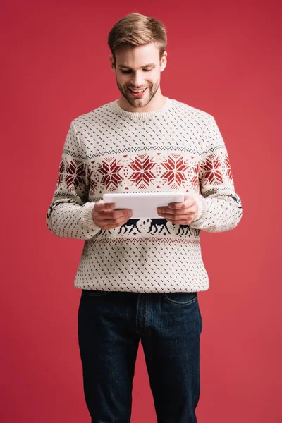 Hombre sonriente guapo en suéter de invierno utilizando tableta digital aislado en rojo - foto de stock