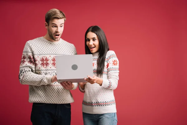 Ударная пара в зимних свитерах с помощью ноутбука, изолированного на красный — стоковое фото