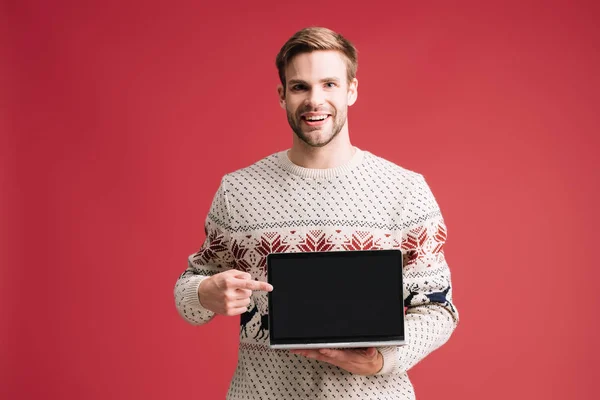Hombre guapo apuntando a la computadora portátil con pantalla en blanco aislado en rojo - foto de stock