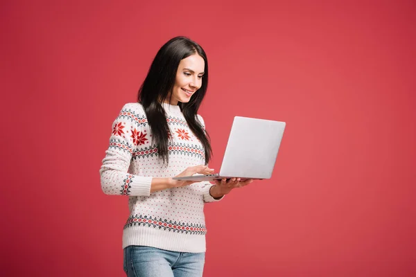 Femme heureuse en pull d'hiver en utilisant un ordinateur portable isolé sur rouge — Photo de stock