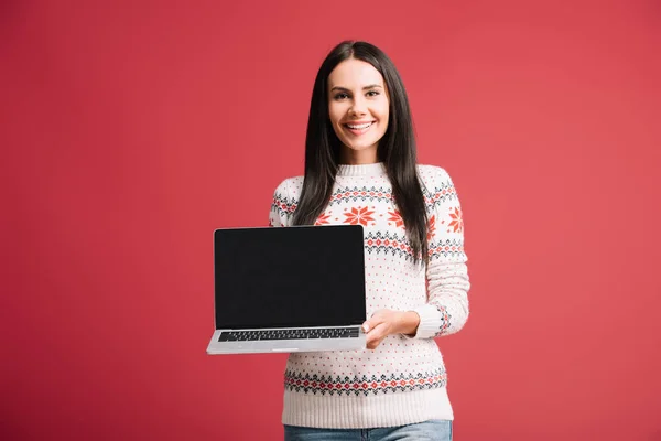 Happy woman in winter sweater showing laptop with blank screen isolated on red — Stock Photo