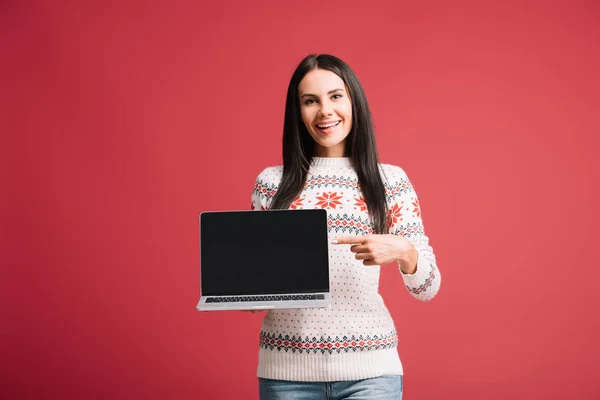 Beautiful woman in winter sweater pointing at laptop with blank screen isolated on red — Stock Photo