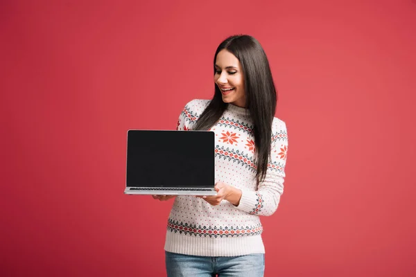 Sorridente ragazza in maglione invernale mostrando laptop con schermo bianco isolato sul rosso — Foto stock