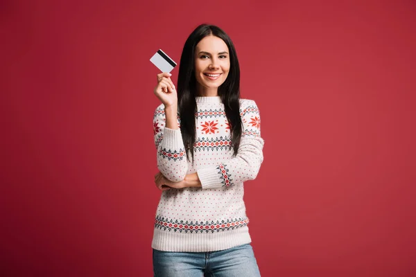 Femme souriante en pull d'hiver tenant la carte de crédit, isolé sur rouge — Photo de stock