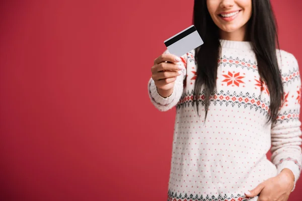 Vue recadrée de la femme en pull d'hiver tenant carte de crédit, isolé sur rouge — Photo de stock