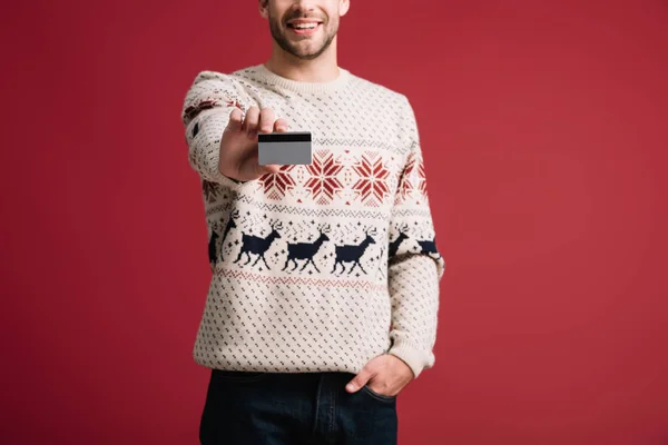 Vista ritagliata dell'uomo in maglione invernale mostrando carta di credito, isolato su rosso — Foto stock