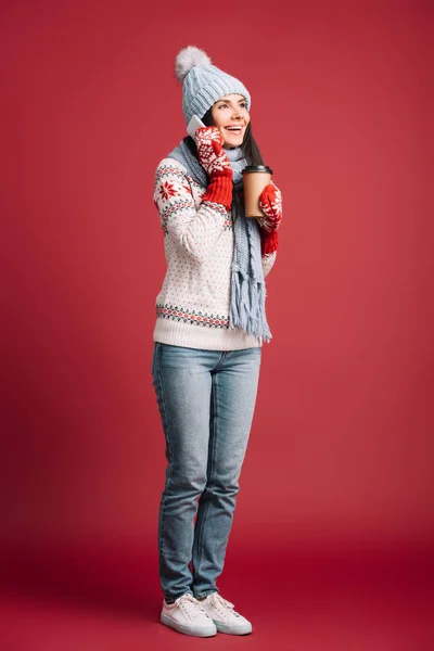 Femme heureuse en chapeau d'hiver parlant sur smartphone et tenant le café pour aller isolé sur rouge — Photo de stock