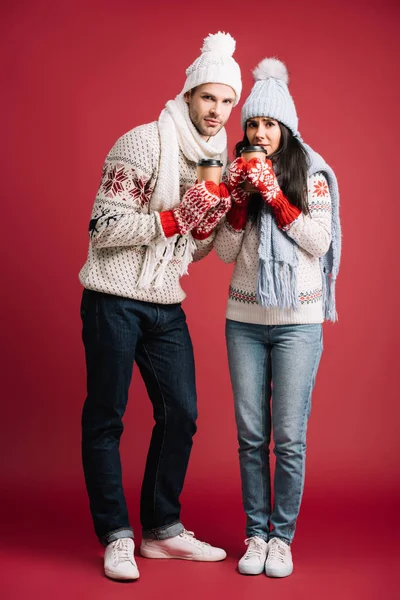 Couple in winter sweaters, hats, scarves and mittens holding coffee to go isolated on blue — Stock Photo