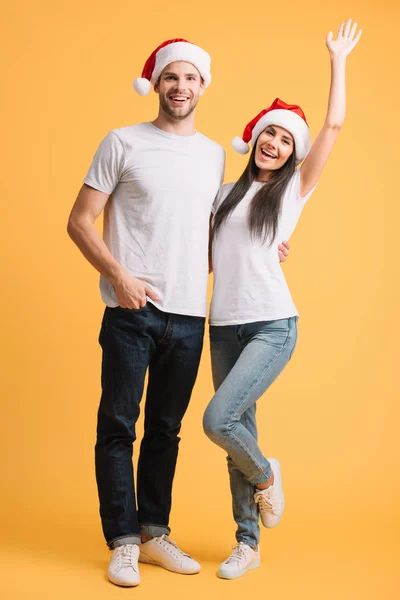 Excited couple in santa hats having fun on yellow — Stock Photo
