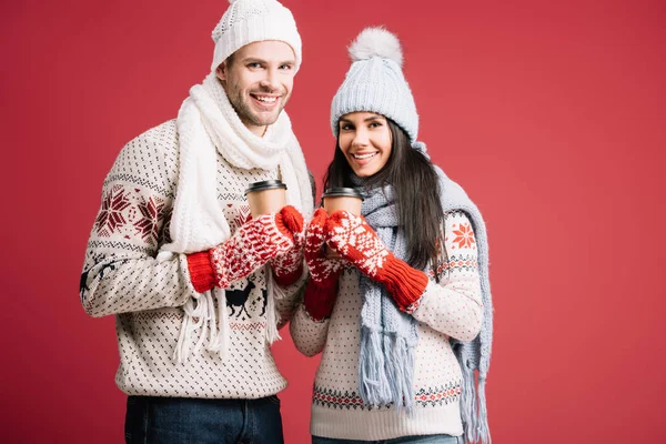 Smiling couple in sweaters, hats, scarves and mittens holding coffee to go isolated on blue — Stock Photo