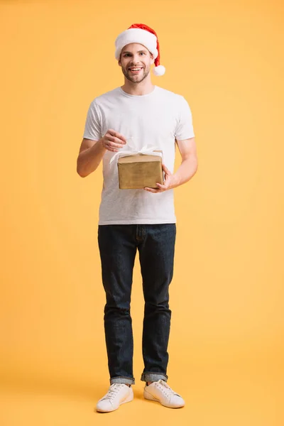 Красивый мужчина в шляпе Санты держит рождественский подарочный коробок изолирован на желтый — стоковое фото