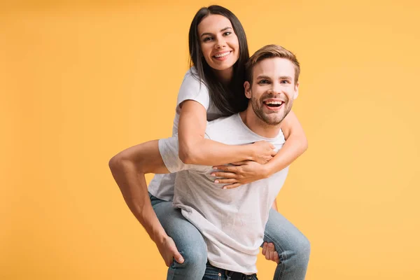 Hermosa feliz pareja piggybacking en blanco camisetas, aislado en amarillo — Stock Photo