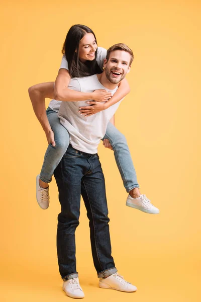 Feliz hombre piggybacking su novia, aislado en amarillo - foto de stock