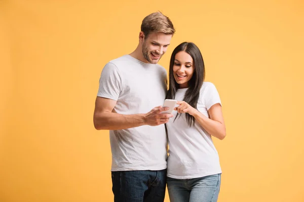 Casal sorrindo usando smartphone isolado no amarelo — Fotografia de Stock