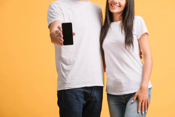 Vista recortada de pareja mostrando smartphone con pantalla en blanco aislado en amarillo - foto de stock