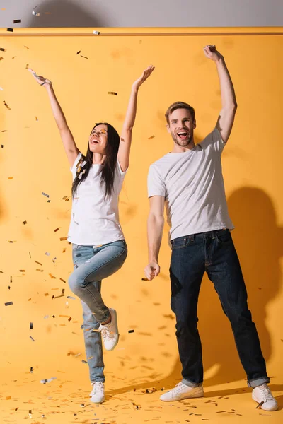 Casal animado dançando no amarelo com confete dourado — Fotografia de Stock