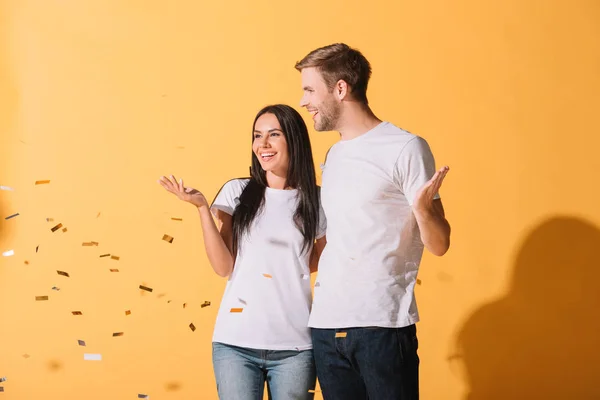 Belo casal abraçando no amarelo com confete dourado — Fotografia de Stock