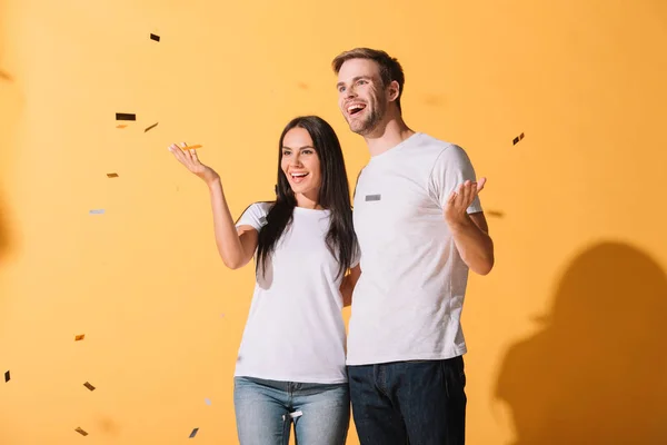 Happy couple hugging on yellow with golden confetti — Stock Photo