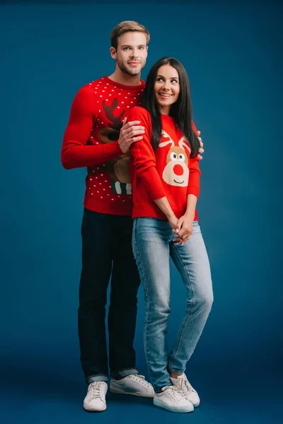 Happy couple in christmas sweaters hugging isolated on blue — Stock Photo