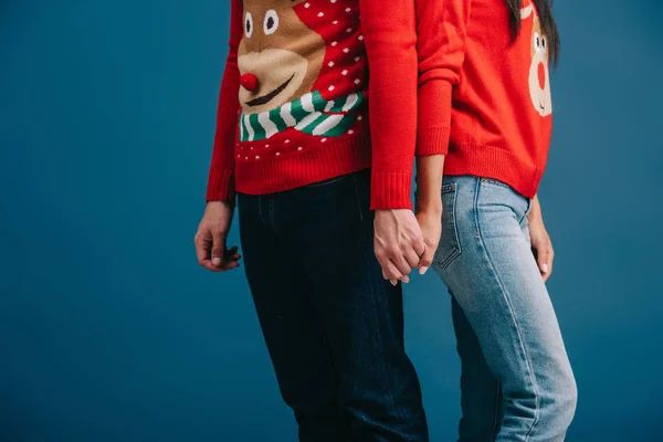 Vista recortada de la pareja en suéteres de Navidad tomados de las manos aislados en azul - foto de stock