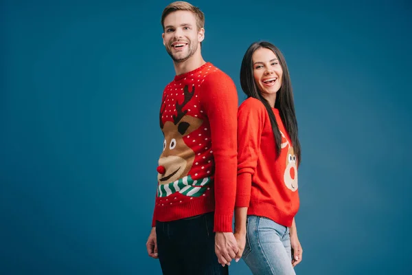 Sonriente pareja en navidad suéteres cogidos de la mano aislados en azul - foto de stock