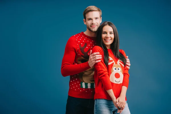 Beautiful happy couple in christmas sweaters hugging isolated on blue — Stock Photo