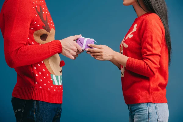 Cropped view of couple in red sweaters holding christmas present isolated on blue — Stock Photo