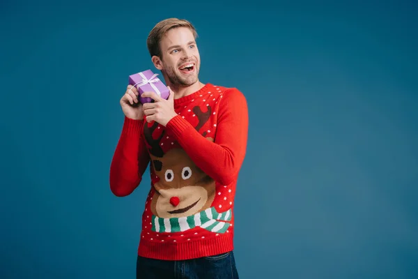Homme heureux en pull tenant cadeau de Noël isolé sur jaune — Photo de stock