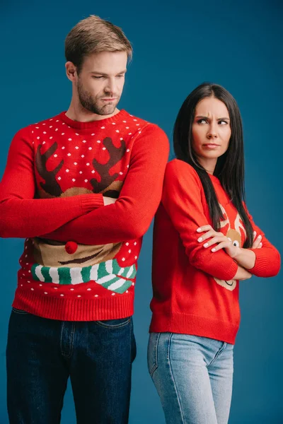 Оскорбленная пара в рождественских свитерах стоящих со скрещенными руками изолированными на голубом — стоковое фото