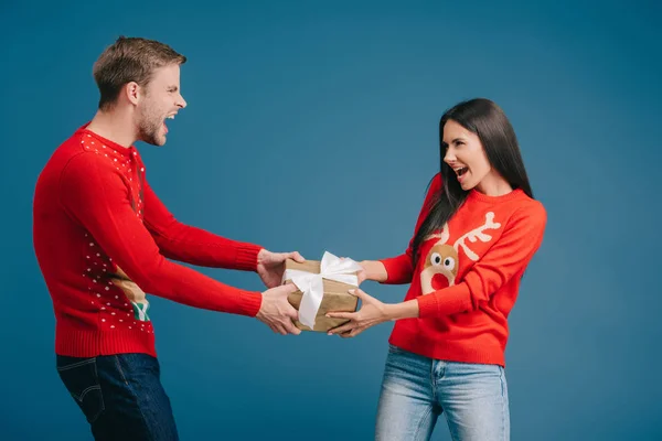 Couple shouting and pulling christmas gift isolated on blue — Stock Photo